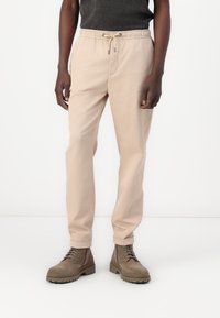 Pantalon en mélange de coton beige avec une taille élastique et un cordon de serrage. Coupe droite avec des revers, associé à des bottes en cuir beige à lacets.