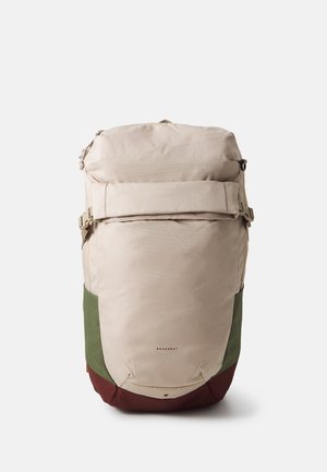 Mochila con tapa enrollable beige, verde y marrón con hebillas laterales y bolsillo frontal con cremallera, etiquetada "Doughnut" en el centro delantero.