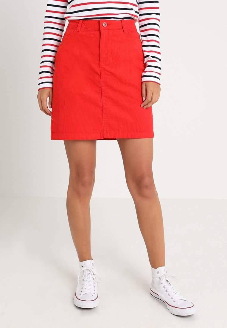 Jupe trapèze en velours côtelé rouge avec fermeture à boutons à l'avant, présentant une texture lisse et une coupe au niveau du genou, assortie à des baskets montantes blanches.