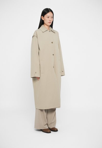Μπεζ υπερμεγέθη παλτό με καμπυλωτό γιακά, κουμπί μπροστά κ�αι πλαϊνές τσέπες. Συνδυάζεται με μπεζ παντελόνι φαρδιάς γραμμής και καφέ παπούτσια.