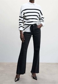 Suéter acanalado a rayas blancas y negras, de manga larga, con cuello alto, combinado con jeans negros de cintura alta y con campana y tacones puntiagudos negros.