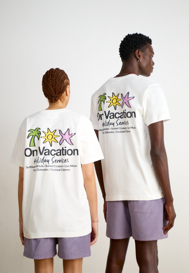 Weiße Baumwoll-T-Shirts zeigen bunte Grafiken von Palmen, einer Sonne und einem Seestern auf dem Rücken, mit dem Text „Urlaubsdienstleistungen“.