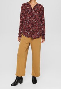 Rød og sort blomster langærmet bluse med V-udskæring, parret med beige vidde bukser og sorte ankel støvler. Glat stof og afslappet pasform.