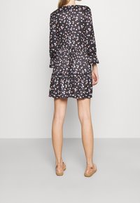 Robe noire à fleurs avec des manches longues, un ourlet en étages, ornée de petites fleurs multicolores. Associée à des sandales espadrilles rose clair.