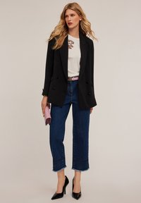 Zwarte dubbelgeknoopte blazer over een witte blouse met geborduurd detail, gecombineerd met cropped, afgescheurde denim. Zwarte lakleren hakken en een roze clutch.