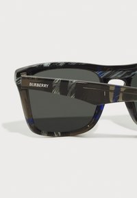 Ochelari de soare Burberry cu un cadru cu model negru și albastru, lentile întunecate și un detaliu de bradă pe tige. Fabricati din material plastic ușor.