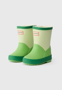 Bottes en caoutchouc vertes avec une texture lisse, présentant une tige vert clair et une semelle vert foncé, étiquetées "HUNTER" à l'avant.