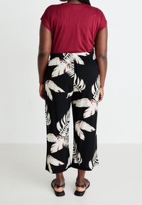 Bordeaux krátký rukáv top v kombinaci s černými kalhotami culottes s bílým a vínovým potiskem listů. Modelka má na sobě ploché černé sandály.
