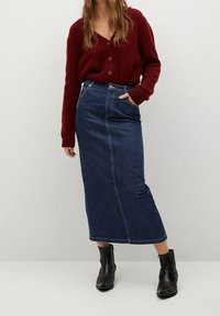 Burgundin neulecardigan, jossa on kolme nappia, yhdistettynä tummansinisestä denimistä valmistettuun midi-hameeseen, jossa on suora leikkaus ja näkyvät tikkausdetails. Mustat nilkkurit.