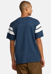 T-shirt à manches courtes bleu marine avec des accents rayés blancs sur les manches, col rond et ourlet droit. Fabriqué en coton doux.