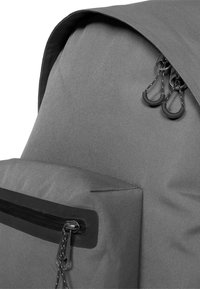 Šedý batoh vyrobený z texturované látky, s horním klopou, zipovou kapsou a dvojitými zipy s gumičkovými úchyty.