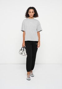 Gray oversized t-shirt with short sleeves, black sweatpants, silver flat shoes, and a small black-and-white Puma handbag.