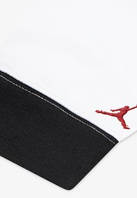 White fabric with black accents and red Jumpman logo. Feature a textured cuff and contrasting stitching along the seam.