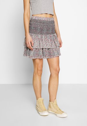 Mujer con minifalda acampanada de estampado y cintura fruncida, top gris corto y zapatillas altas beige, posando contra un fondo blanco.