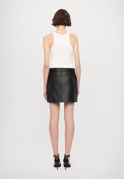 Gonna mini in pelle nera con un design aderente, cuciture orizzontali e una vita; abbinata a un top bianco senza maniche e scarpe nere con tacco alto.