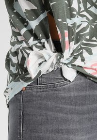 Knyttröja i grön, vit och rosa blommönster; mjukt tyg; avslappnad passform; matchas med mörkgrå jeans som visar låg midja.