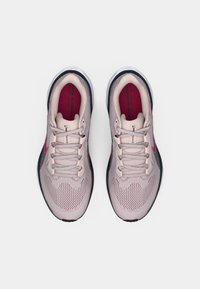 Une paire de baskets de course Nike rose clair avec un design à lacets et des semelles noires, vue de dessus sur un fond blanc.