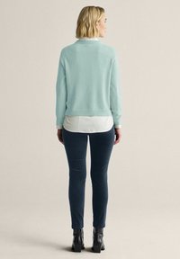 Ljusblå tröja med rund halsringning, bärs över en vit skjorta, tillsammans med mörkblå skinny jeans och svarta klackboots.