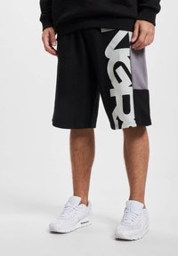 Black shorts with gray accents and large white lettering on the side. Worn with white sneakers, featuring a mesh and suede design.