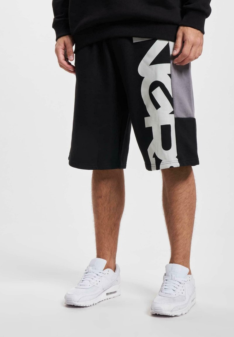 Black shorts with gray accents and large white lettering on the side. Worn with white sneakers, featuring a mesh and suede design.
