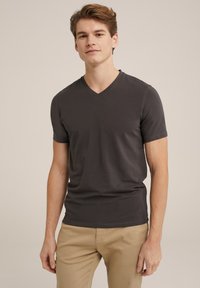 Camiseta gris de cuello en V en un diseño ajustado, hecha de tela suave con mangas cortas, combinada con pantalones beige. Apariencia simple y limpia.