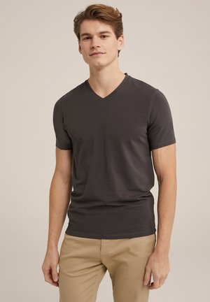 Camiseta gris de cuello en V en un diseño ajustado, hecha de tela suave con mangas cortas, combinada con pantalones beige. Apariencia simple y limpia.
