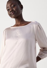 Light pink blouse with a boat neckline, three-quarter puff sleeves, and gathered cuffs. Smooth texture with subtle seam detailing.