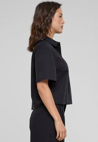 Camicia nera a maniche corte con bottoni in vestibilità rilassata. Tessuto morbido, senza fantasie, orlo dritto e design del colletto classico.
