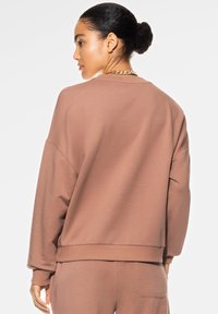 Mauve oversized sweatshirt met afhangende schouders en ribgebreide manchetten, met een zachte textuur en een eenvoudig, minimalistisch ontwerp.