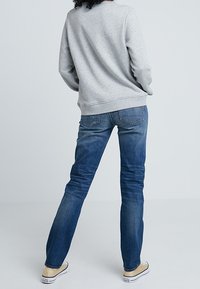 Grijze sweatshirt met geribbelde manchetten en zoom, gecombineerd met mid-blauwe denim jeans met achterzakken en een lichte vervaging. Neutraal gekleurde sneakers.