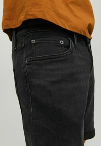 Șorturi din denim negre cu tiv răsucit, având cinci buzunare și închidere cu nasture. Purtați cu un tricou bej deschis dintr-un material moale.