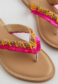 Sandalai su flip-flop stiliumi, tan spalvos padas, rožinė fringing juosta ir dekoratyviniai karoliukai geltonos ir auksinės spalvos. Su piršto įdėklu ir siuvinėtu apdailu.