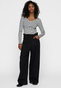 Maglietta a maniche lunghe a righe in bianco e nero, abbinata a pantaloni neri a gamba larga con cintura elasticizzata e tasche. Tessuto morbido.