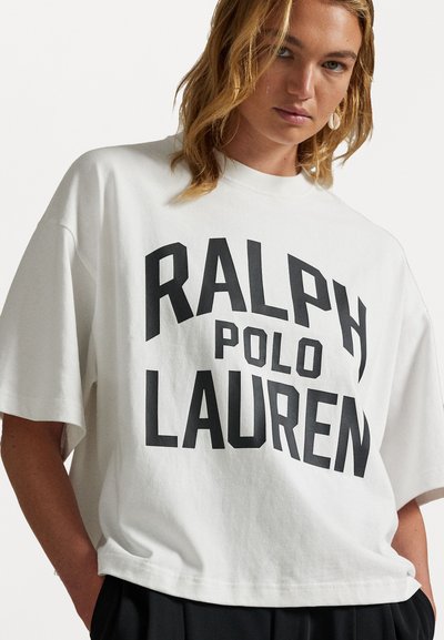 Baltais, pārāk liels kokvilnas T-krekls ar izteiksmīgu melnu tekstu "RALPH POLO LAUREN" blokveida fontā. Īsas piedurknes un brīva piegriezuma.