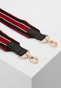 Proplétaný pásek v červené, černé a růžové barvě s kovovými klipy ve zlaté tónině a černými koženými detaily. Plochý, silný design s výraznými pruhy.