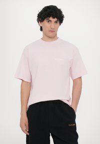 Light pink cotton t-shirt with short sleeves, round neckline, and white "No Problemo" text on the chest. Worn with black sweatpants.