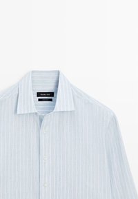 Chemise habillée pour hommes bleu clair avec de subtiles rayures verticales et des boutons blancs, présentée à plat avec un col pointu.