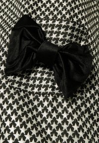 Svart tyg med metallisk silverstjärnmönster; har ett stort svart satinrosettaccent. Slät textur, skräddarsydd design och fickdetalj.