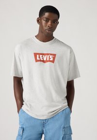 Camiseta de algodão cinza com um logo vermelho da Levi's no peito. Apresenta um decote redondo e mangas curtas. Adequada para uso casual.