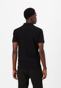 Polo preto com colarinho, mangas curtas e corte reto. Textura suave, usado com calças pretas risca-de-giz.