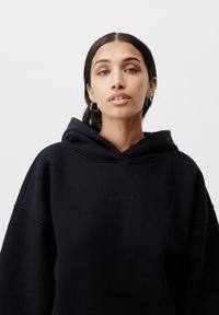Felpa con cappuccio nera realizzata in un morbido tessuto, con un logo in rilievo discreto sul petto e una vestibilità rilassata con maniche ampie.