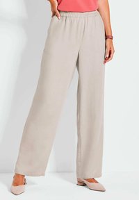 Beige wijde broek met een elastische tailleband en zijzakken, gemaakt van gladde stof. Gepaard met lichtroze schoenen.