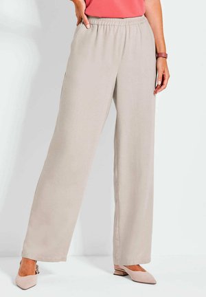 Beige wijde broek met een elastische tailleband en zijzakken, gemaakt van gladde stof. Gepaard met lichtroze schoenen.
