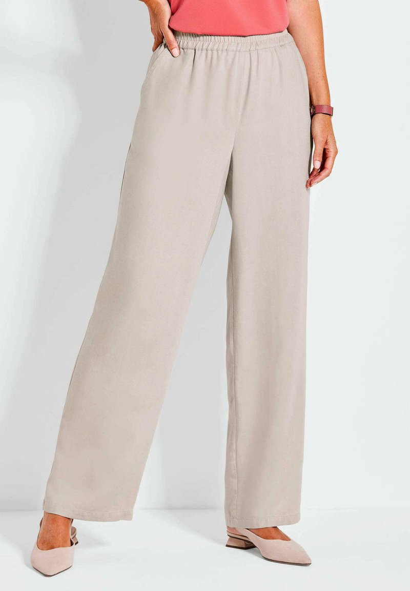 Beige wijde broek met een elastische tailleband en zijzakken, gemaakt van gladde stof. Gepaard met lichtroze schoenen.
