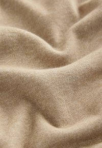 Beżowy materiał o miękkiej, teksturowanej powierzchni, prezentujący łagodne zakładki i gładkie, lekko błyszczące wykończenie, podkreślające ciepły odcień.