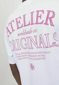 Bijela pamučna majica s intenzivnim ružičastim natpisom na leđima: "ATELIER worldwide co. ORIGINALS" uz dodatne brending i dizajnerske detalje.