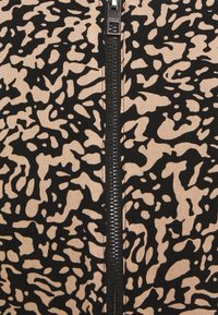 Tissu à motifs noirs et beiges avec un design abstrait, fermeture éclair centrale avec tirette en métal, aspect lisse et texturé.