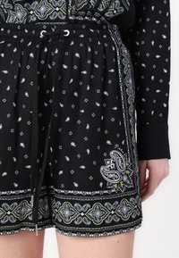 Svarte shorts med hvite paisley- og geometriske mønstre; har en snor i livet; stoffet ser lett ut med en glatt tekstur.