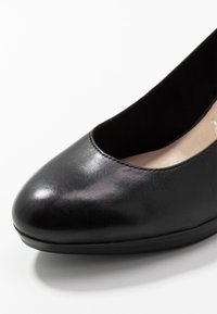 Černé kožené dámské baleríny s zaoblenou špičkou a hladkým zakončením na bílém pozadí.