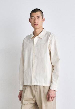 Camisa de botones color crema con rayas verticales, hecha de tela ligera, con un cuello clásico y una textura suave.